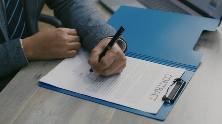 Signing a music contract agreement with pen and blue folder on table