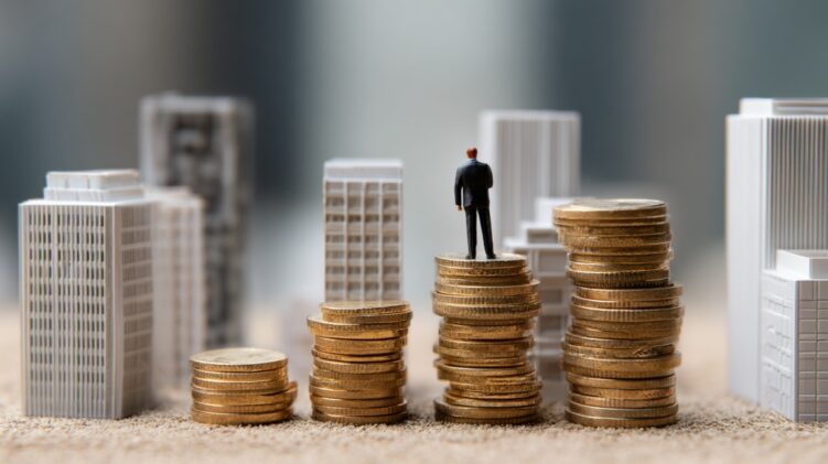 Small figurine standing on stacked coins among miniature city buildings
