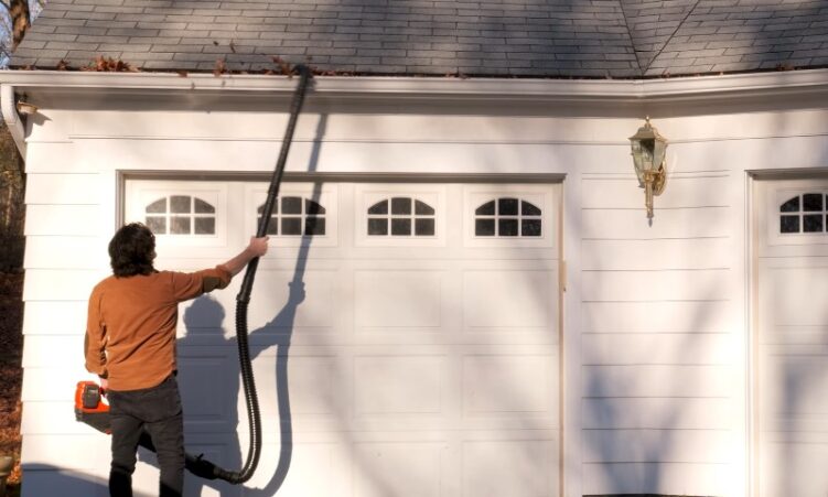 A man operates a leaf blower to clear debris from the floor of a garage